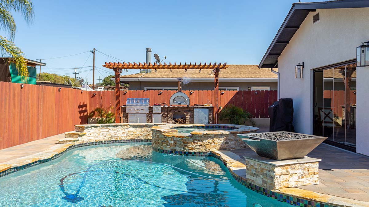 Luxury outdoor kitchen with pizza oven beside a backyard pool