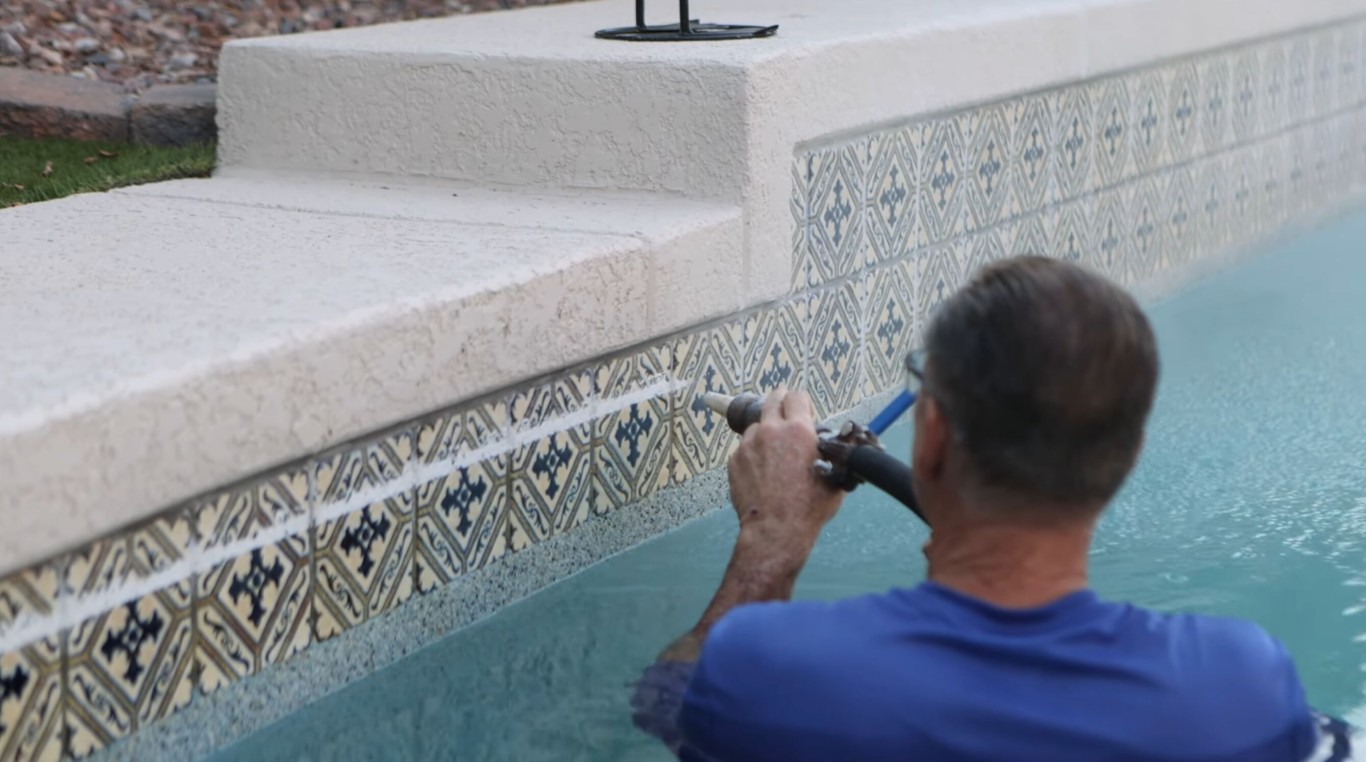 Technician cleaning swimming pool tile and removing calcium buildup